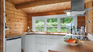 A modern kitchen with wooden walls, a large window, and a central island with a bowl of fruit. - Stunning home in Skibby with WiFi (Skibby)