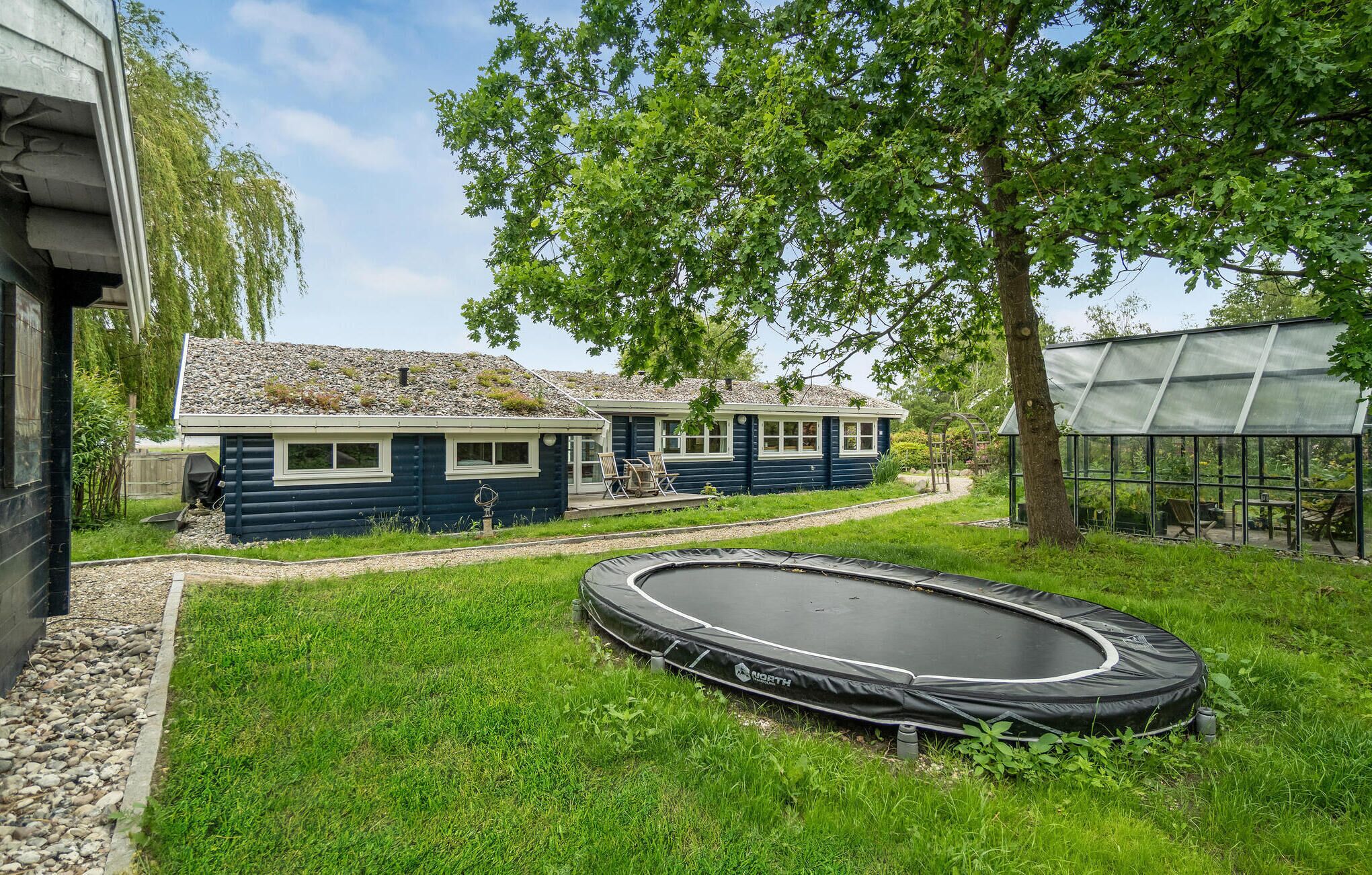 A house with a small garden, a trampoline, and a greenhouse.