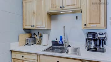 Una kitchenette con gabinetes de madera, un tostador, una cafetera y un lavamanos.