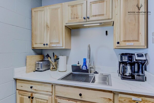 A kitchenette with wooden cabinets, a toaster, a coffee maker, and a sink.