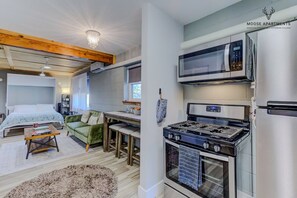 A compact living space with a kitchenette, a bed with a headboard, a dining area, and a fireplace.