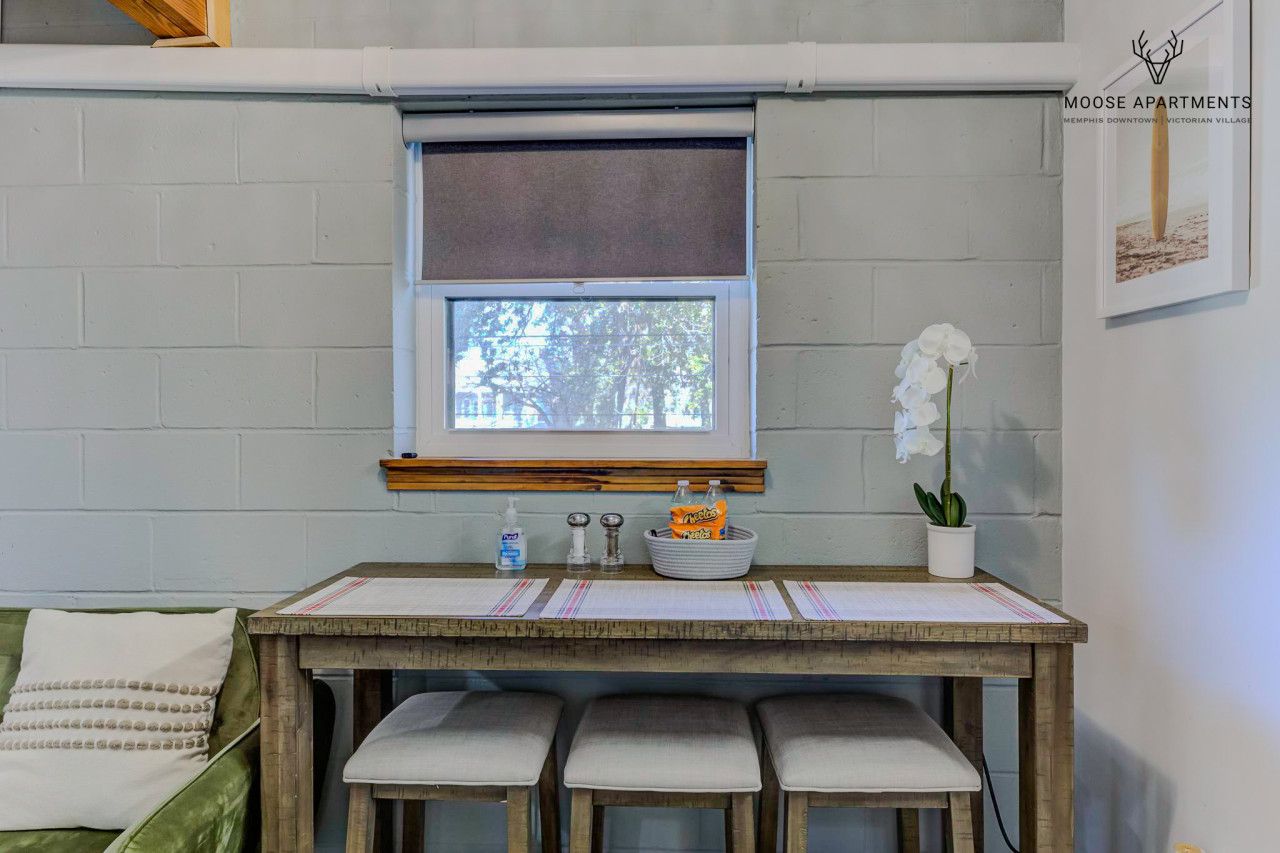 A small kitchenette with a window, a table with chairs, and a potted plant.