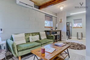 Una sala moderna con un sofá verde, una mesa de centro de madera y una cocina al fondo.