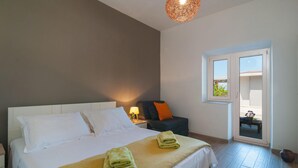 Ett hotellrum med en säng, ett nattduksbord med en lampa, en stol och ett fönster med utsikt över omgivningen.