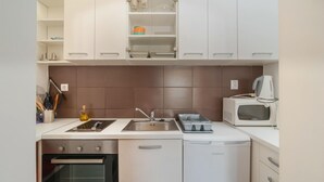 Ett kompakt kök med en inbyggd ugn, en mikrovågsugn, en diskho och en diskmaskin.