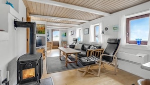 Een gezellige woonkamer met een houtkachel, een eethoek en uitzicht op de omgeving.