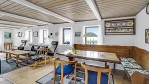 Een ruime woonkamer met een houten eettafel, meerdere stoelen, een bank en uitzicht op de omgeving door grote ramen.