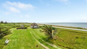 Een kustpand met een huis met rieten dak, een gazon, een pad en uitzicht op zee.
