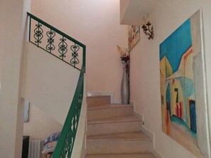 A staircase with a green handrail, a vase with flowers, and a colorful abstract painting on the wall.