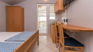 Quarto compacto com cama, guarda-roupa de madeira, escrivaninha com cadeira e televisão na parede.