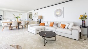 A modern living room with a sectional sofa, a round coffee table, and a dining area with a table and chairs. - Panorama | pool - terrace - sea views (Fuengirola)