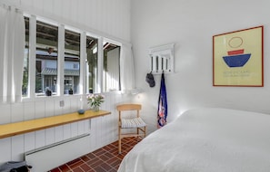 A bedroom with a bed, a window with curtains, a small table with a vase, a chair, and a wall-mounted radiator. - Lovely apartment in Allinge with WiFi (Allinge)