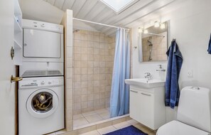 A compact bathroom with a washing machine, a shower, a sink, and a toilet. - Lovely apartment in Allinge with WiFi (Allinge)