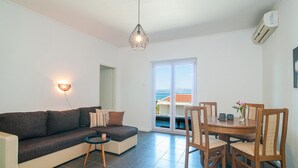 Ett modernt vardagsrum med en soffa, ett litet runt bord och en matplats med stolar. Det finns ett stort fönster med utsikt över havet.