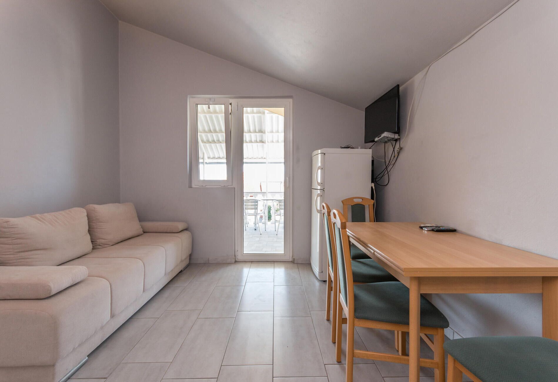 Un espacio habitable compacto con un sofá, una mesa de comedor con sillas, un refrigerador y un televisor montado en la pared.