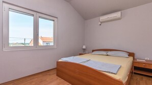 Een slaapkamer met een houten bed, een nachtkastje, een lamp en een raam met uitzicht op gebouwen.