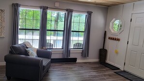 En moderne stue med en mørk sofa, et spisebord og et stort vindue med gardiner.