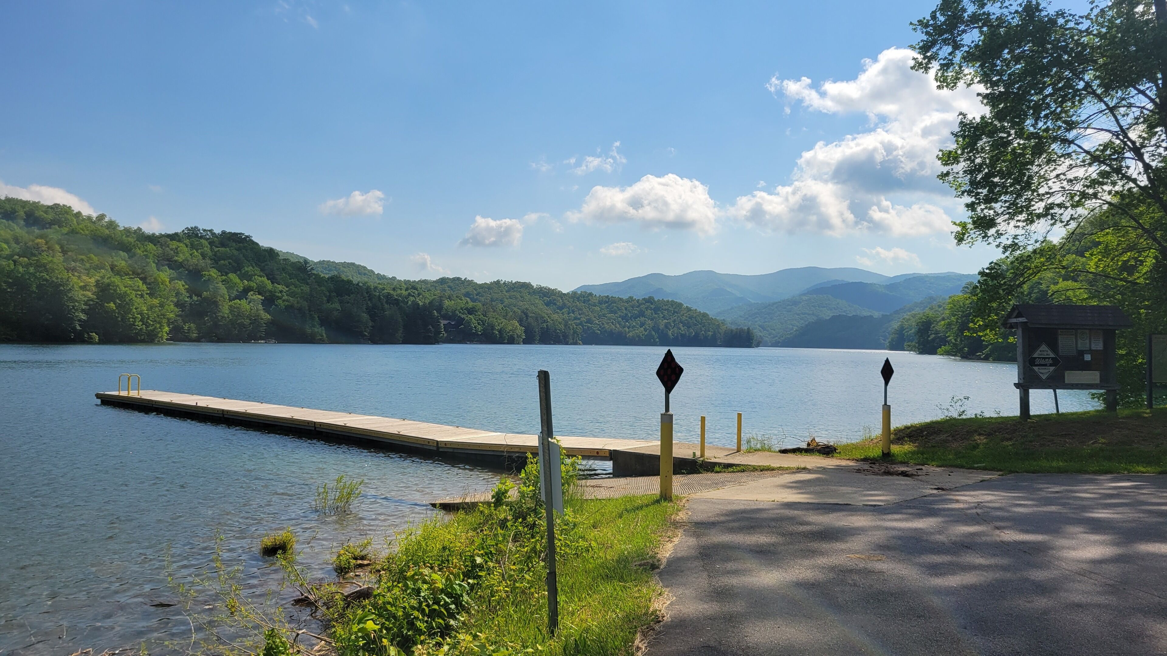 Un muelle al borde de un lago tranquilo, rodeado de exuberante vegetación y montañas al fondo.