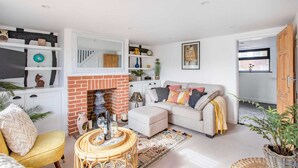 A cozy living room with a fireplace, a sofa, a yellow armchair, and a coffee table. - Stunning Character 2bed Cottage in St Albans Wifi (St Albans)