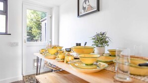 A dining area with a long table set with yellow bowls and plates, a potted plant, and a framed picture on the wall. - Stunning Character 2bed Cottage in St Albans Wifi (St Albans)