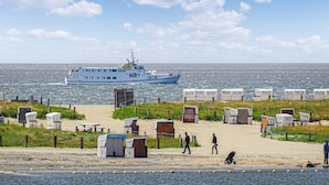 A beach with portable cabins, a boat in the water, and a sandy area with people and a stroller. - Beautiful home in Büsum with sauna (Büsum)