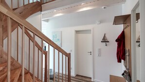 A wooden staircase leading to a room with a door, a wall-mounted light fixture, and a red garment hanging on a hook. - Beautiful home in Büsum with sauna (Büsum)