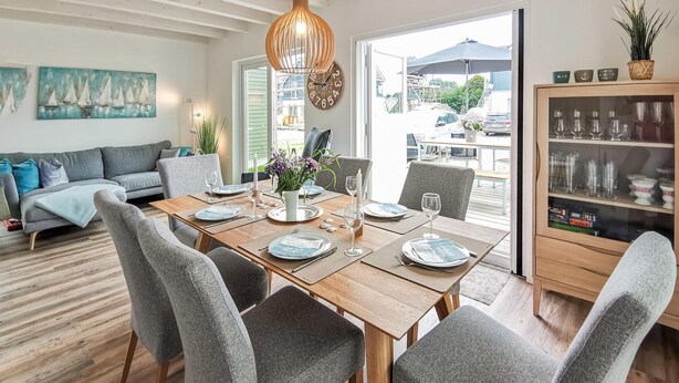 A dining area with a wooden table set for four, grey upholstered chairs, a vase with flowers, and a clock on the wall. - Beautiful home in Büsum with sauna (Büsum)