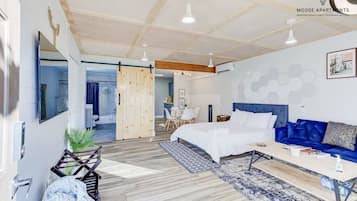 Une chambre moderne avec un lit, un canapé bleu, un plancher en bois et une grande fenêtre.