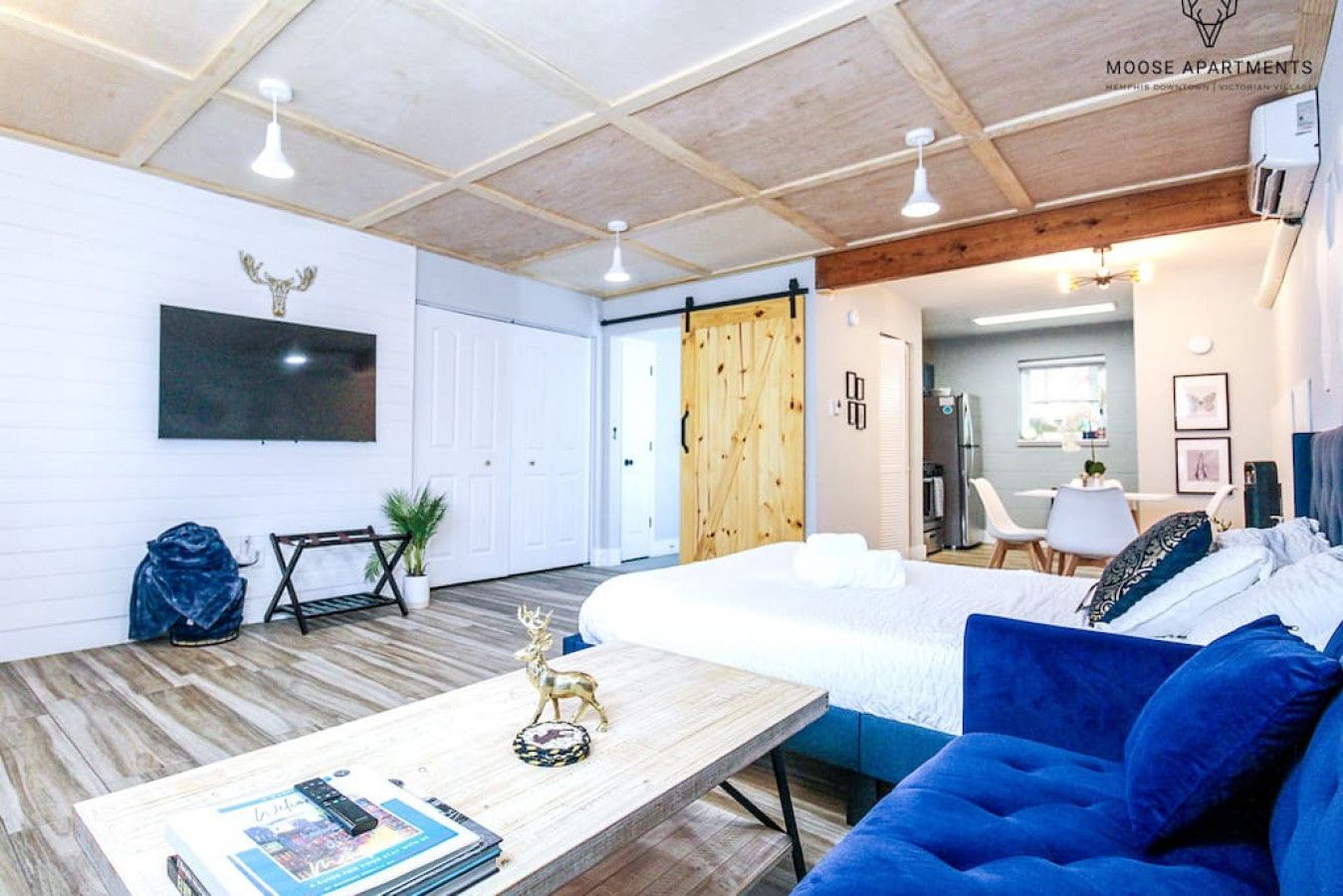 A modern living room with a large bed, a wooden coffee table, and a TV mounted on the wall.