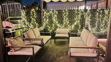 An outdoor seating area with four cushioned chairs and a table, surrounded by a decorative wall of lights.