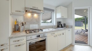 Une cuisine moderne avec des armoires blanches, des appareils en acier inoxydable et une fenêtre donnant sur une terrasse.