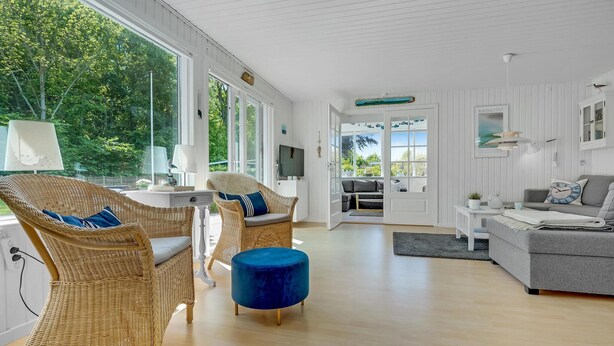 Ein heller, offener Wohnbereich mit Rattanmöbeln, einem blauen Hocker und einem grauen Sofa.