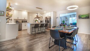 A modern kitchen with white cabinets, a central island with bar stools, and a dining area with a wooden table and chairs. - Entire home remodeled & 1 mile to Kenai River & 1/2 block to Peninsula Hospital (Soldotna)