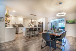 A modern kitchen with white cabinets, a central island with bar stools, and a dining area with a wooden table and chairs. - Entire home remodeled & 1 mile to Kenai River & 1/2 block to Peninsula Hospital (Soldotna)