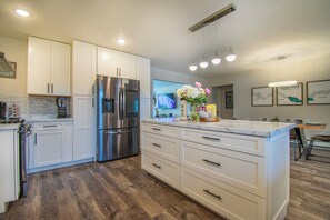 A modern kitchen with white cabinets, a stainless steel refrigerator, and a wooden floor. - Entire home remodeled & 1 mile to Kenai River & 1/2 block to Peninsula Hospital (Soldotna)