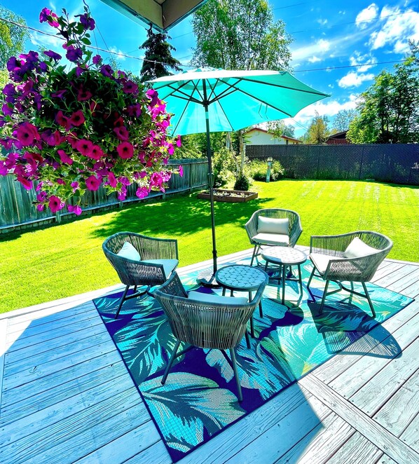 Eine Terrasse mit Gartenmöbeln, einem großen Sonnenschirm und einem Blumenbeet.