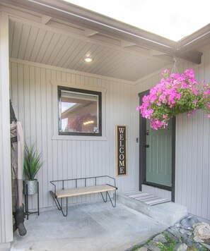A porch with a bench, a welcome sign, a hanging flower basket, and a door. - Entire home remodeled & 1 mile to Kenai River & 1/2 block to Peninsula Hospital (Soldotna)