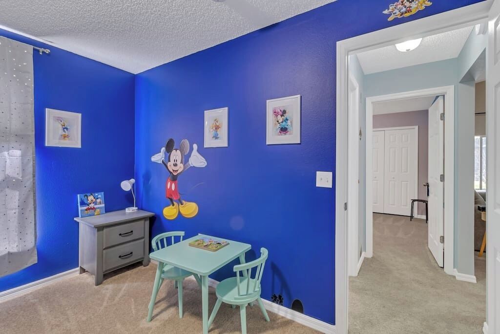 Una habitación con paredes azules, un mural de Mickey Mouse, un escritorio con cajones y una mesa con sillas.