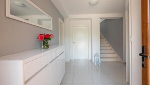 Un couloir avec un comptoir blanc, un vase de fleurs, un miroir et un escalier.