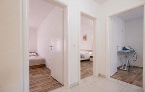Een hotelkamer met een bed, een nachtkastje en een klein bureau met een stoel. Er is een deur die naar een andere kamer leidt.