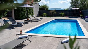Une piscine rectangulaire, entourée d’une terrasse carrelée, avec des chaises longues et des parasols.