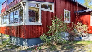 A red wooden house with white-framed windows and a small garden area with plants and a potted plant.