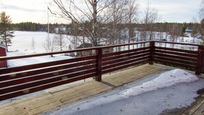 A wooden deck with a metal railing overlooking a snowy landscape with trees and buildings in the background.