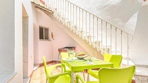 Un área luminosa para comer al aire libre con una mesa, sillas, una escalera y una ventana.