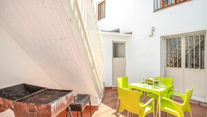 Un patio con una parrilla, sillas de color amarillo brillante y una mesa lista para comer.