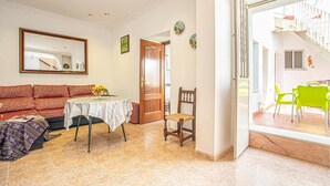 Un salón con un sofá, una mesa de comedor con un cuenco de fruta, una silla de madera y una escalera que conduce a un espacio al aire libre con una silla verde.