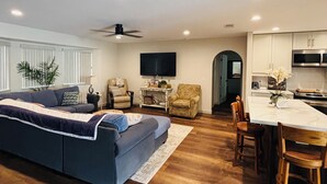 A modern living room with a sofa, armchairs, a TV, and a dining area with a table and chairs.