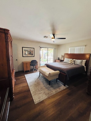 Un dormitorio con cama, escritorio, silla, armario de madera y ventilador de techo.