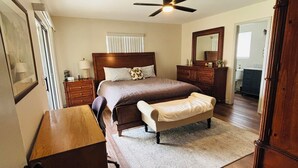 A bedroom with a bed, a wooden dresser, a bench, a ceiling fan, and a mirror.
