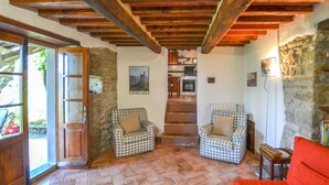 Uma sala de estar acolhedora com parede de pedra, teto de madeira, sofá xadrez, poltrona vermelha e escada que dá para uma cozinha.